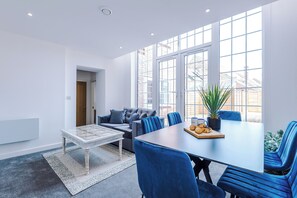 A modern room with a dining table, blue chairs, a sofa, and a large window. - Middleton Chambers by Guestz (Hull)