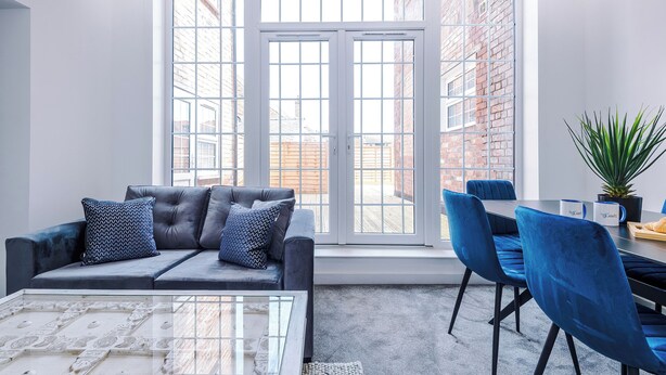 A modern room with a sofa, chairs, a glass coffee table, and a large window with a view of a brick building. - Middleton Chambers by Guestz (Hull)