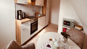 A compact kitchen with a coffee maker, sink, and stove. There is a dining area with a table and chairs. - Vacation apartment "Utkiek" in Greetsiel (50 sqm / 2-3 persons) (Krummhörn)