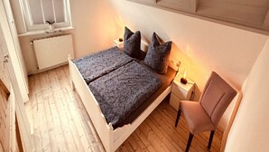 A bedroom with a bed, a chair, a nightstand, a window, and a radiator. - Vacation apartment "Utkiek" in Greetsiel (50 sqm / 2-3 persons) (Krummhörn)