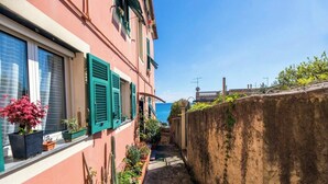A narrow alleyway with a building on the left, a stone wall on the right, and a clear view of the sea in the background. - Beach 1Min | Sea View| 2BR| A/C| by Tilo (Genoa)