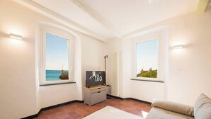 A modern living room with large windows, a flat-screen TV, and a sofa. - Beach 1Min | Sea View| 2BR| A/C| by Tilo (Genoa)