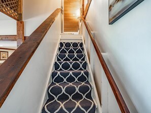 A staircase with a geometric patterned carpet, wooden handrails, and a wooden floor.