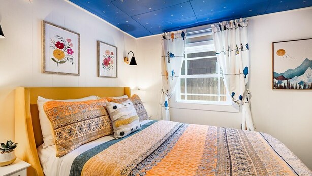 A bedroom with a bed, a nightstand, a window with curtains, and wall art. - Boho Blue Heron, BBH 7532 (Birch Bay)