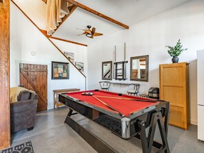 A pool table in a room with a wooden ceiling, a sofa, a cabinet, and a staircase. - Boho Blue Heron, BBH 7532 (Birch Bay)