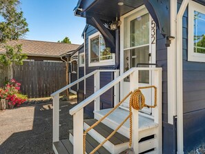 A small, single-story building with a porch and a wooden fence in the background. - Boho Blue Heron, BBH 7532 (Birch Bay)