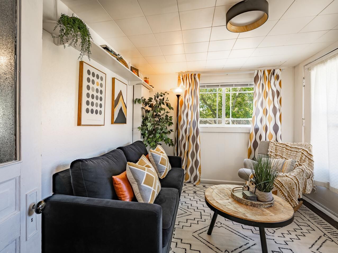 A living room with a black sofa, patterned cushions, a round coffee table, and a chair with a woven seat.