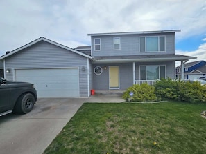 A two-story house with a garage, a front yard with grass and bushes, and a parked SUV.