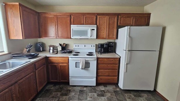 A kitchen with wooden cabinets, a white stove, a microwave, and a refrigerator. - Spacious Family Home w Garage  Gladys Retreat (Hermiston)
