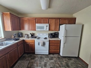 A kitchen with wooden cabinets, a white stove, a microwave, and a refrigerator.