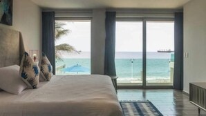 Een slaapkamer met een groot bed, uitzicht op de oceaan en een schip in de verte.