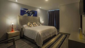 Een moderne hotelkamer met een groot bed, een nachtkastje met lamp, een schilderij aan de wand en uitzicht op buiten.