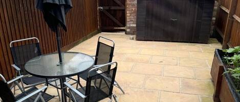 A patio with a round table and chairs, a covered umbrella, and a wooden fence.