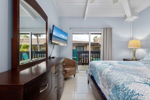 Un dormitorio con cama, televisor, cómoda y balcón con vista a la playa.