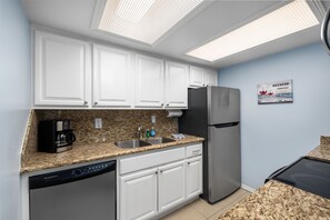 Una cocina con armarios blancos, un refrigerador de acero inoxidable, una cafetera y un lavavajillas.