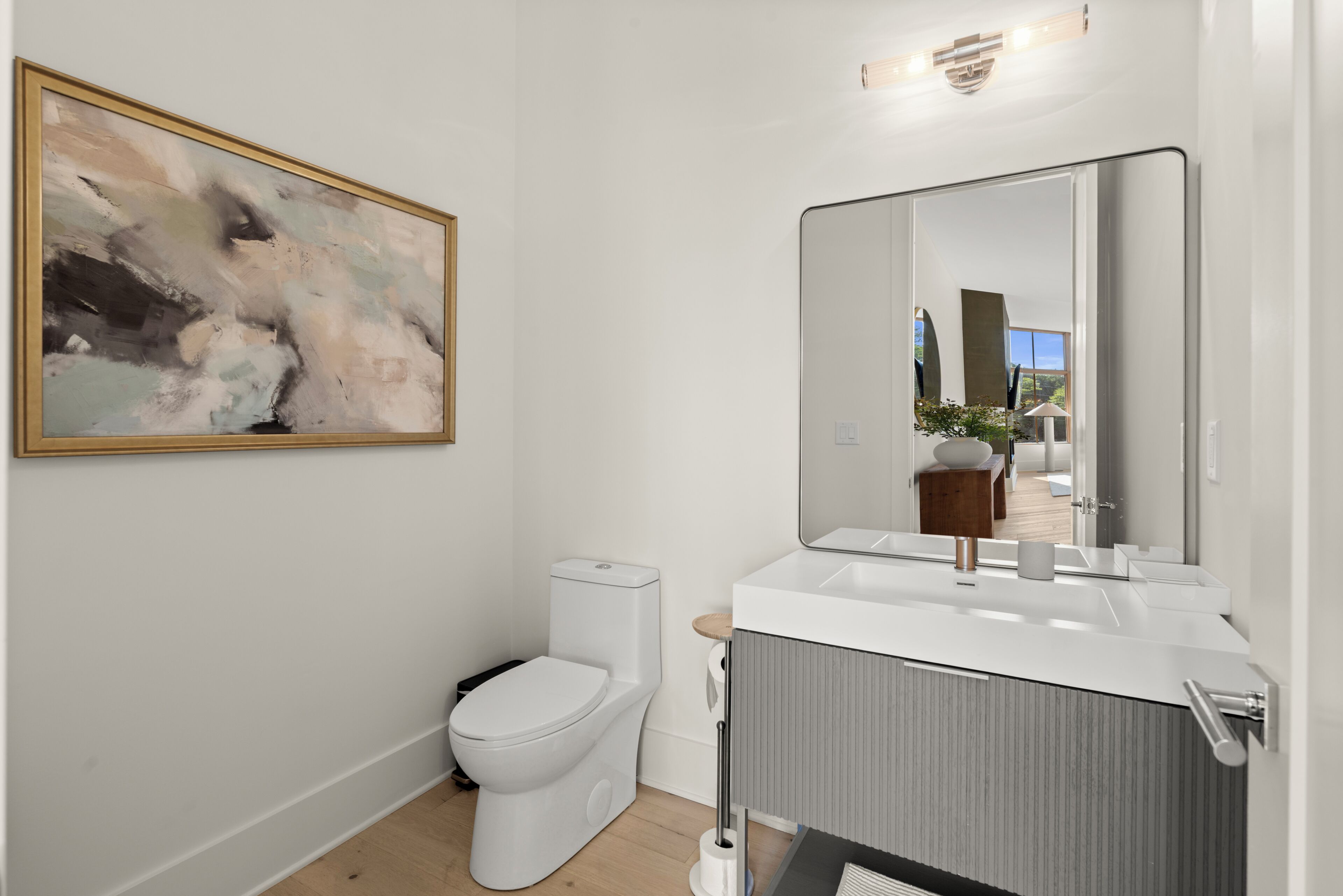 Un baño moderno con inodoro, lavamanos, espejo y un cuadro abstracto en la pared.
