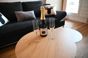 Eine Weinflasche und zwei Gläser auf einem runden Holztisch in einem Wohnzimmer mit einer schwarzen Couch und einem Kissen in Form eines Rehs.