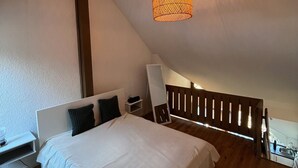 Ein Schlafzimmer mit Bett, Nachttisch, Lampe und einer geneigten Decke mit Pendelleuchte.