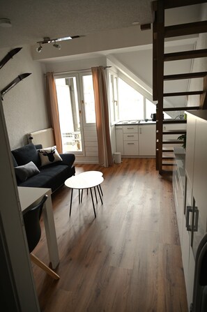 Ein modernes Wohnzimmer mit einer Couch, einem kleinen runden Tisch und einer Küchenzeile mit Schränken und einer Arbeitsplatte.