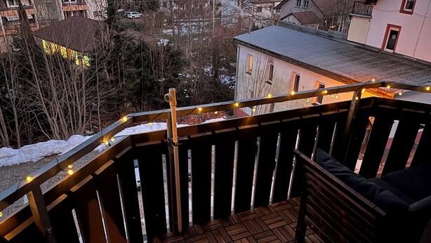 Eine Holzdielen-Terrasse mit Geländer, einer Bank und Lichterketten.