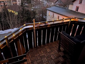 Eine Holzdielen-Terrasse mit Geländer, einer Bank und Lichterketten.