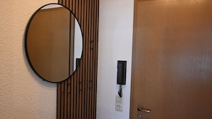 Ein Zimmer mit einer Wand aus Holzlamellen, einem runden Spiegel, einer Tür und einer Leuchte über dem Spiegel.