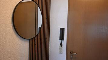 A room with a wooden slat wall, a round mirror, a door, and a light fixture above the mirror.