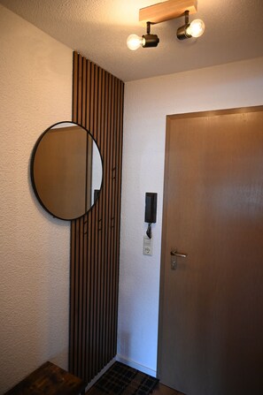 Ein Zimmer mit einer Wand aus Holzlamellen, einem runden Spiegel, einer Tür und einer Leuchte über dem Spiegel.