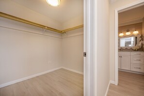 Ein Zimmer mit Holzboden, weißen Wänden, einer Deckenleuchte und einer Tür zu einem Badezimmer mit Waschtisch und Spiegel.
