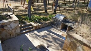 A stone patio with a grill, surrounded by trees and a fenced area. - Spacious 4-bedroom estate in beautiful Spring Branch with AC and gym (Spring Branch)