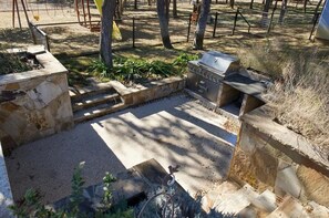 A stone patio with a grill, surrounded by trees and a fenced area. - Spacious 4-bedroom estate in beautiful Spring Branch with AC and gym (Spring Branch)