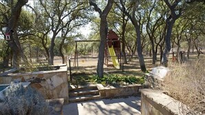 A playground with a slide and climbing structures, surrounded by trees and stone walls. - Spacious 4-bedroom estate in beautiful Spring Branch with AC and gym (Spring Branch)