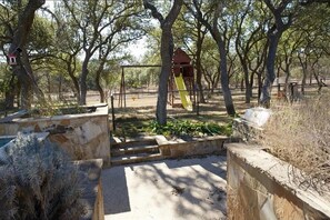 A playground with a slide and climbing structures, surrounded by trees and stone walls. - Spacious 4-bedroom estate in beautiful Spring Branch with AC and gym (Spring Branch)