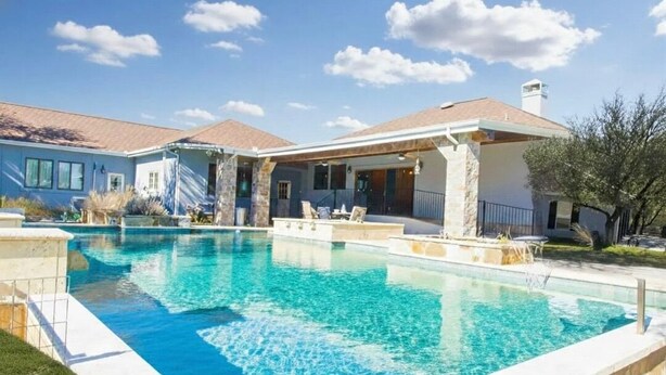 A swimming pool with a stone deck, a covered patio, and a house with a tiled roof. - Spacious 4-bedroom estate in beautiful Spring Branch with AC and gym (Spring Branch)