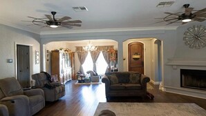 A spacious living room with two sofas, a fireplace, ceiling fans, and a chandelier. - Spacious 4-bedroom estate in beautiful Spring Branch with AC and gym (Spring Branch)