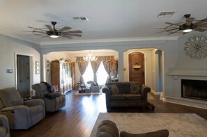 A spacious living room with two sofas, a fireplace, ceiling fans, and a chandelier. - Spacious 4-bedroom estate in beautiful Spring Branch with AC and gym (Spring Branch)