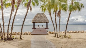 Ein Strand mit einem strohgedeckten Pavillon, Palmen und freiem Blick auf das Wasser.