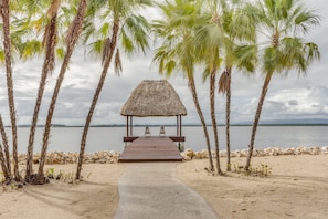 Une plage avec un gazebo à toit de chaume, des palmiers et une vue dégagée sur l’eau.