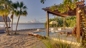 Ein Poolbereich direkt am Strand mit Liegestühlen und einer Pergola.