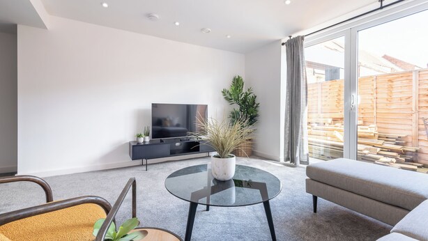 Una sala de estar moderna con un televisor de pantalla plana, una mesa de centro redonda de vidrio, un sofá y una planta en maceta.