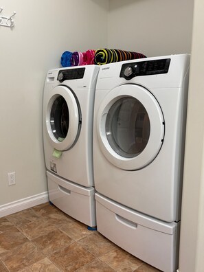 Two stacked front-loading washing machines in a laundry room with a tiled floor. - Garden level suite in sunny Osoyoos. Minutes from beaches, parks and golf! (Osoyoos)