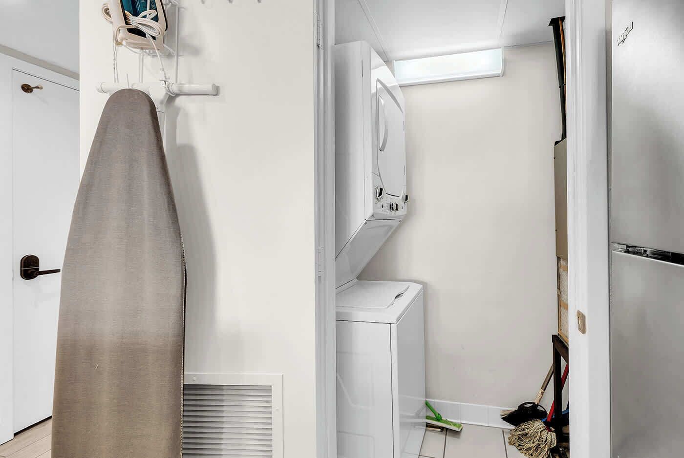 Una habitación con un tendedero, lavadora blanca, espejo y escoba.
