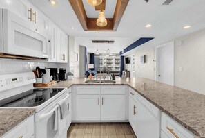 Eine moderne Küche mit weißen Schränken, einer Granit Arbeitsplatte, einem eingebauten Backofen und einer Pendelleuchte.