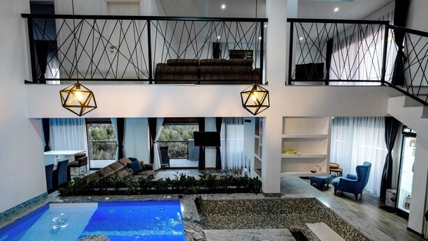 Un'ampia area piscina interna con idromassaggio, una zona relax con divano e poltrone, e una scala che collega due piani.