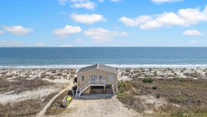 Una casa sulla spiaggia con un portico, una scalinata e vista sull'oceano.