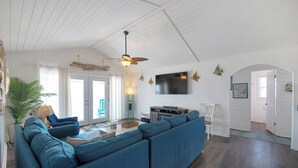 A living room with a sectional sofa, a ceiling fan, a flat-screen TV, and a large window. - Oceanfront, pet friendly, fenced yard (Oak Island)