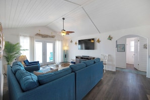 A living room with a sectional sofa, a ceiling fan, a flat-screen TV, and a large window. - Oceanfront, pet friendly, fenced yard (Oak Island)