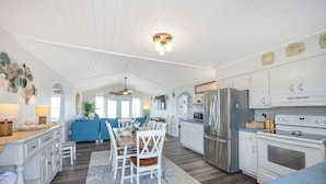 A spacious kitchen with white cabinetry, a dining area with a blue sofa, and a central island. - Oceanfront, pet friendly, fenced yard (Oak Island)