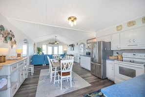 A spacious kitchen with white cabinetry, a dining area with a blue sofa, and a central island. - Oceanfront, pet friendly, fenced yard (Oak Island)