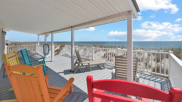 A wooden deck with chairs and a table, overlooking the beach. - Oceanfront, pet friendly, fenced yard (Oak Island)